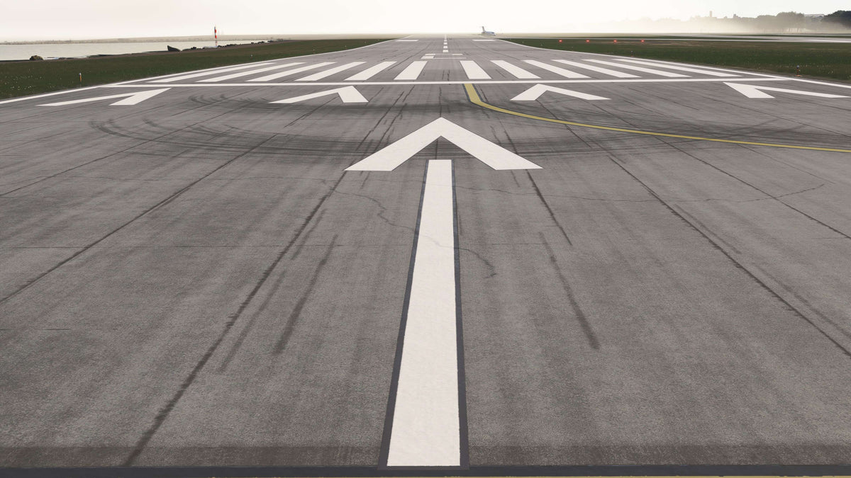 KBKL runway displaced-threshold arrows, white threshold bars and weathered pavement beside Lake Erie in daylight in MSFS.