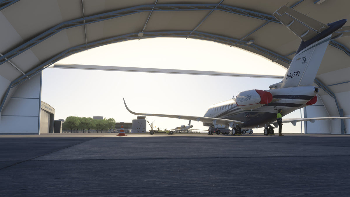 View from inside an arched KBKL hangar past a parked business jet and ground equipment toward the control tower in MSFS.