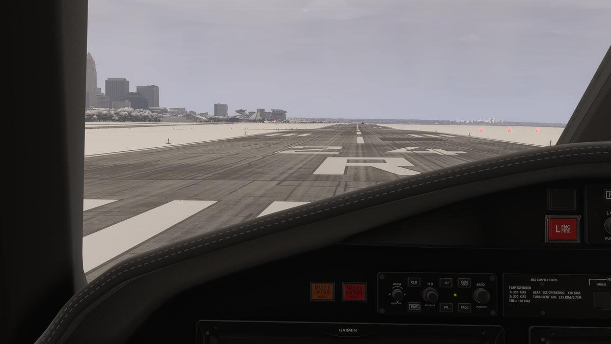 Cockpit view along runway 24R at KBKL with snow-covered ground beside the runway and the Cleveland skyline beyond in MSFS.