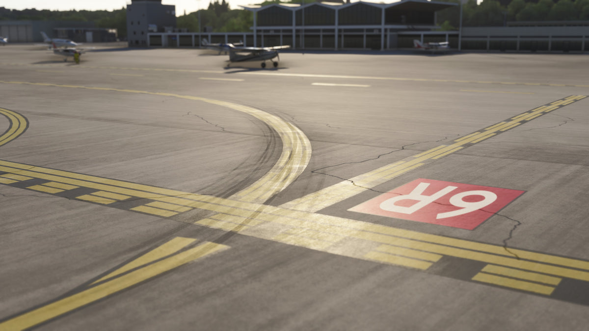 Close-up of a red 6R surface marking, yellow holding lines, tire marks and pavement cracks beside the KBKL apron in MSFS.
